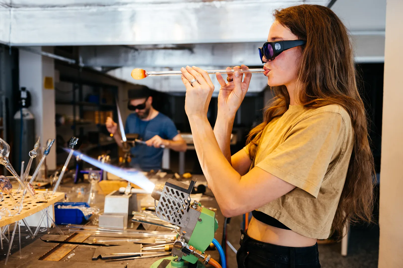 Kvinne som blåser glass i verksted med verneutstyr